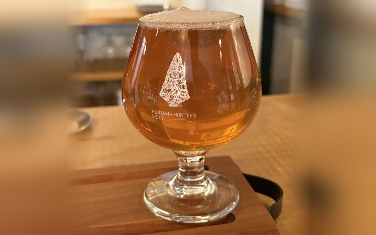 A glass of amber Fujiyama Hunter&rsquo;s craft beer on a wooden serving board at the taproom counter