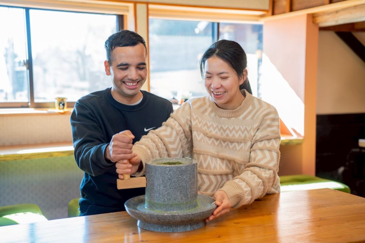 Two guests laughing as they turn a stone mill together to grind tea leaves into matcha at a café