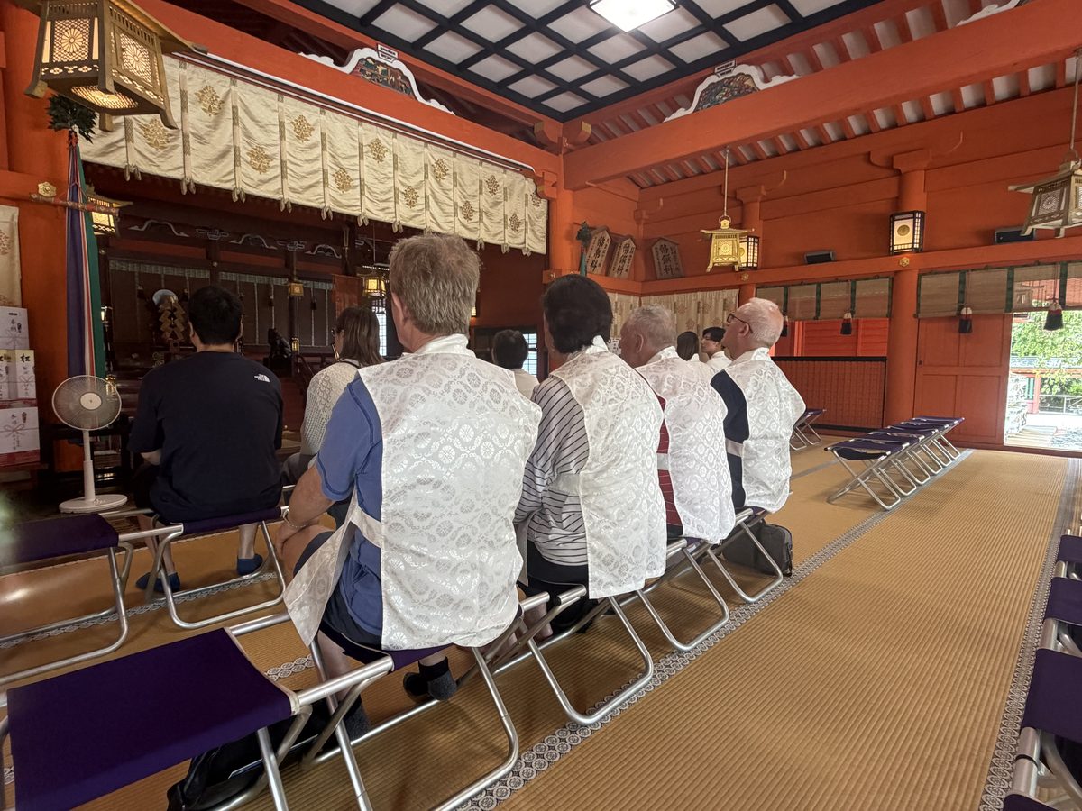 Guests in white vestments receiving a Shinto purification (oharai) prayer inside the shrine hall
