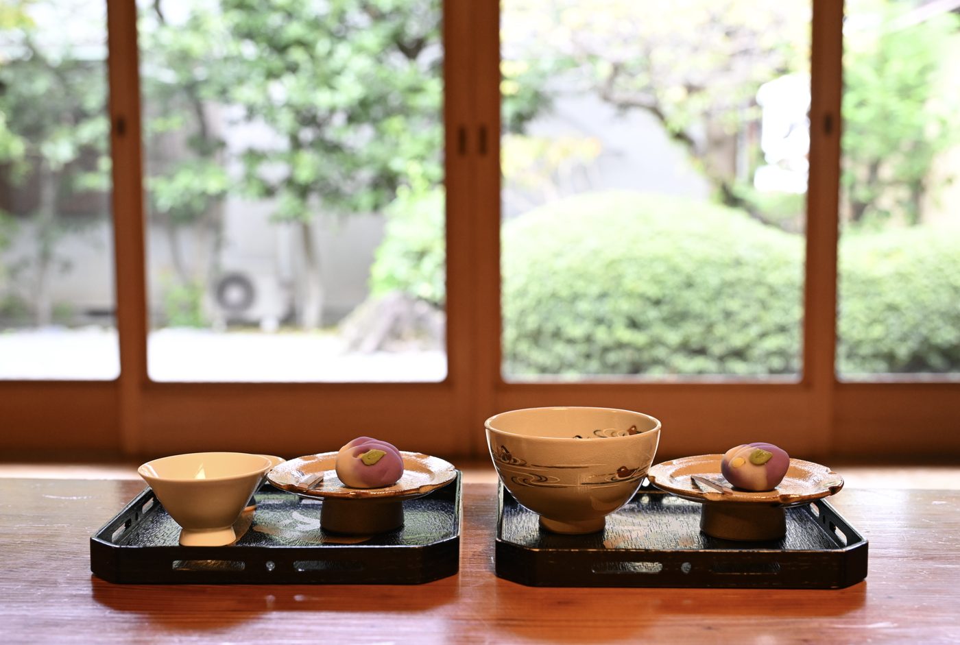 Two tea settings with seasonal sweets on lacquer trays before a garden window at a tea house near Mt. Fuji