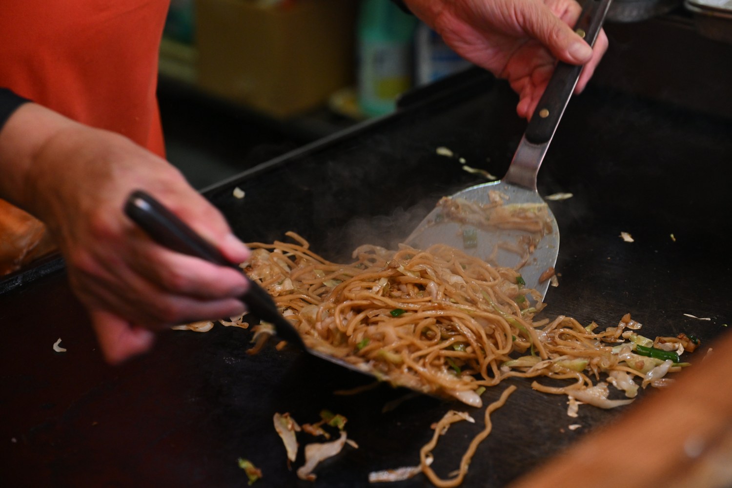 Yakisoba being cooked on a hot griddle with two spatulas