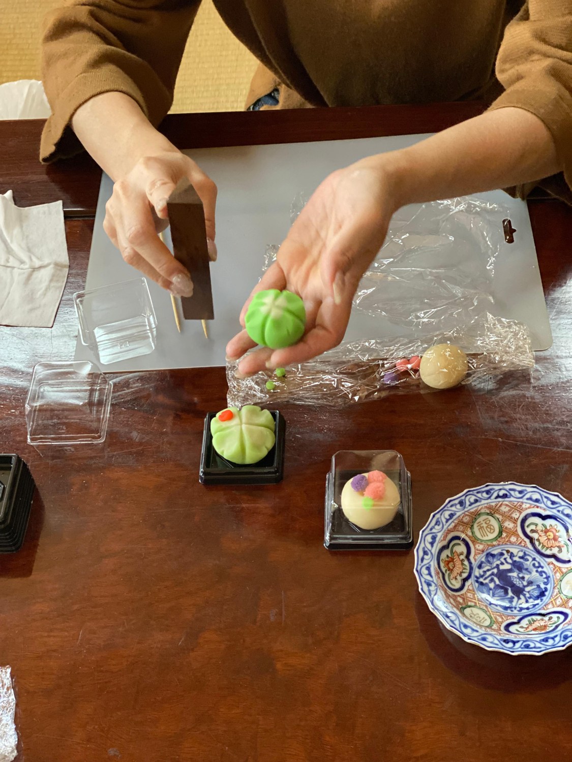 Hands shaping a green Japanese sweet with a wooden tool