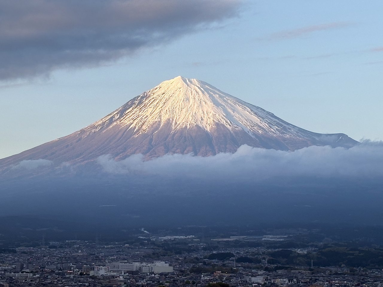 Snow-capped Mt. Fuji glowing at first light above a band of cloud and the town below
